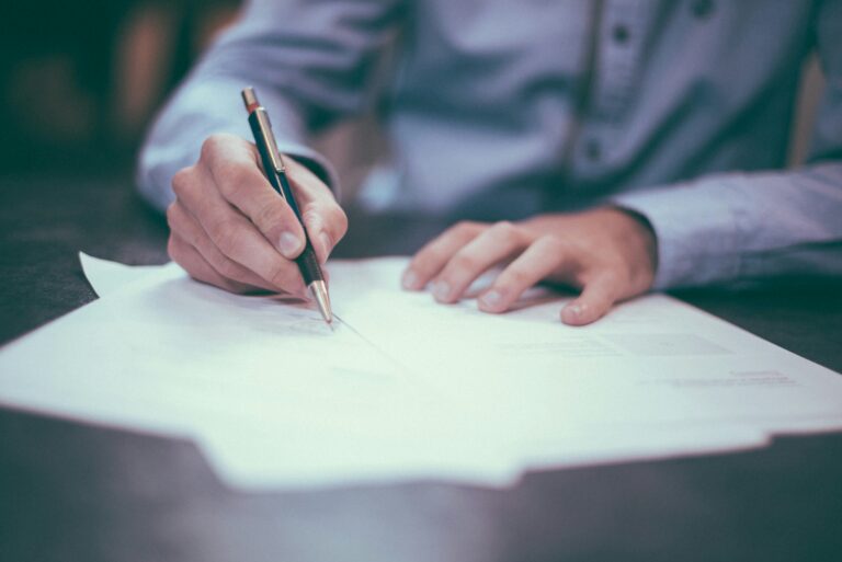 Main d’un homme en train de prendre des notes sur un document, symbolisant la réflexion et la stratégie pour développer son entreprise.